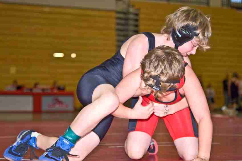 young novice wrestlers, one in a blue onesie and another in a red one.