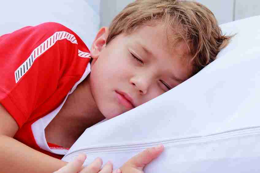 cute 7 years old boy sleeping on white pillow in summer cafe