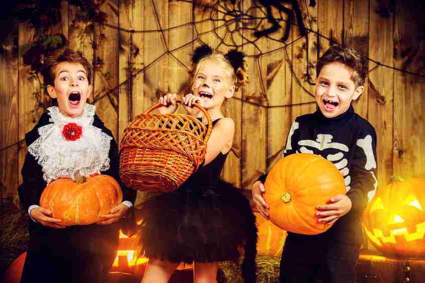 group of joyful children in halloween costumes posing together in a wooden barn with pumpkins. halloween concept.