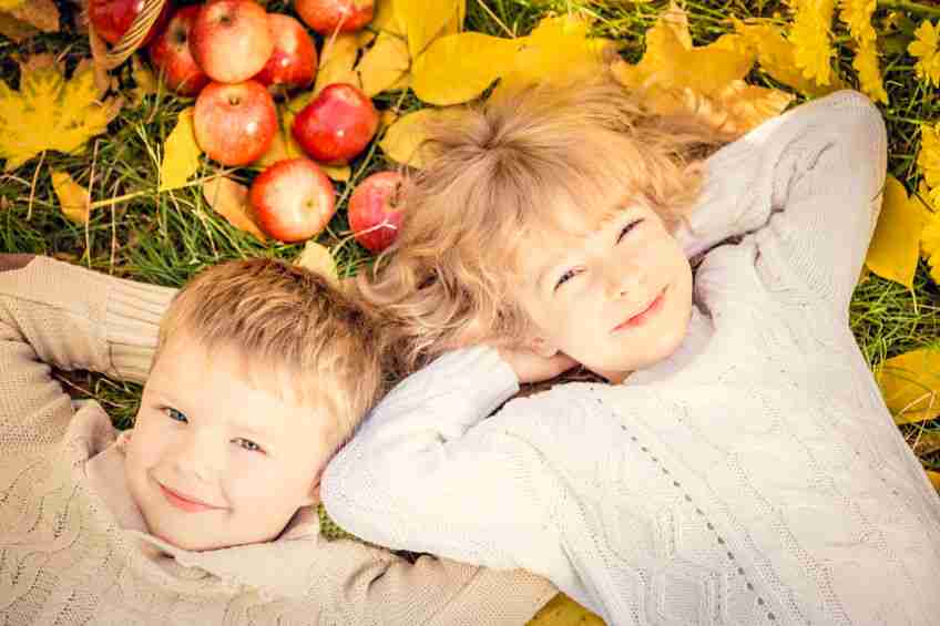 Happy children lying on fall leaves. Funny kids outdoors in autumn park