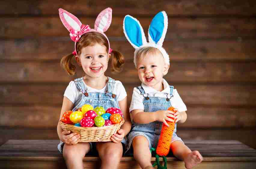 Happy kids boy and girl dressed as Easter bunnies laughing with basket of eggs on wooden background