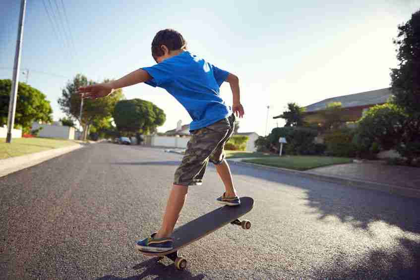 oung boy learning to ride a skateboard on a suburban street, smiling and having fun