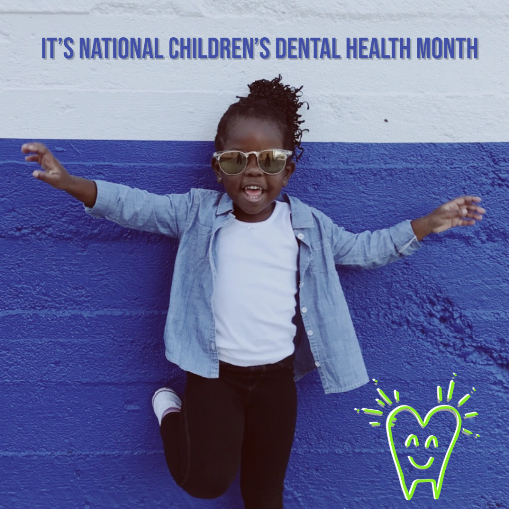 cute african american girl wearing a white top, jean overshirt, and black pants, wearing glasses and standing in from of a wall that is blue/gray on the top and royal blue on the bottom.